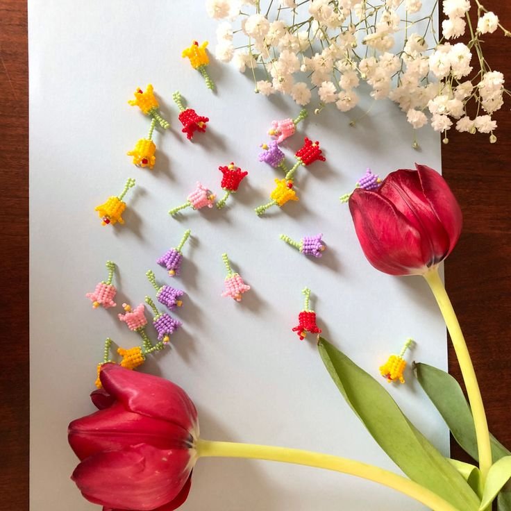 Assortment of colorful beaded flower charms scattered with two tulips and baby's breath flowers.