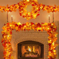 Faux maple leaf garland with warm LED lights draped around a fireplace and on a mantelpiece.