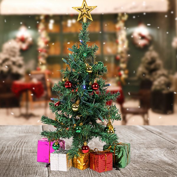 Miniature Christmas tree with multicolor LED lights, ornaments, and a star topper, surrounded by gift boxes on a wooden surface.