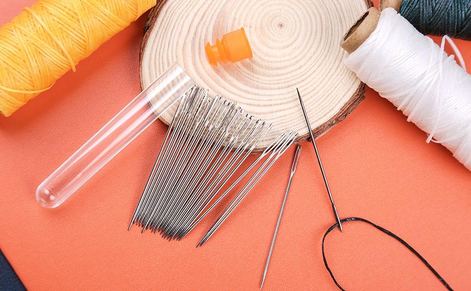 Set of large eye sewing needles with thread spools and a storage tube on an orange surface