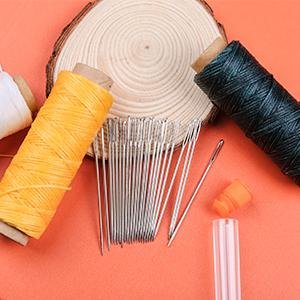 Large eye sewing needles with spools of thread and a storage bottle on an orange background.
