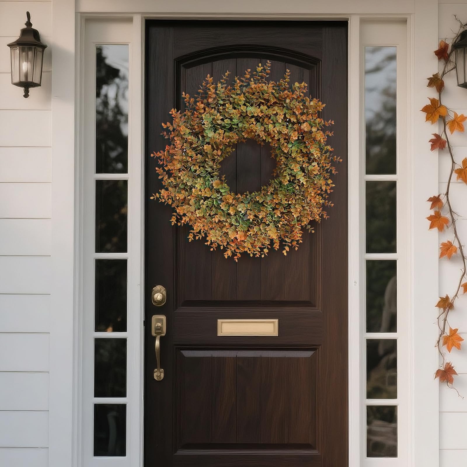 Artificial boxwood fall wreath with green and orange leaves hanging on a dark wood front door.