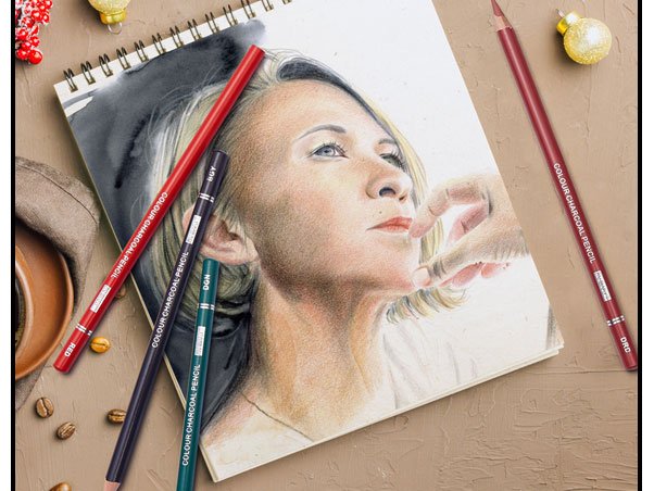 Charcoal pencils and a drawing of a woman's face on a sketchbook, arranged on a textured surface with coffee beans and holiday ornaments.