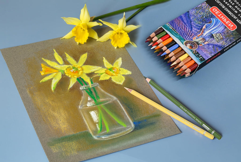 Pastel charcoal pencils in a box next to a drawing of daffodils in a vase and loose daffodils.