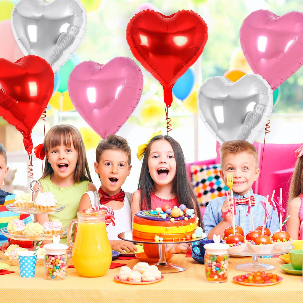 Children at a party table with heart-shaped balloons, cake, and candy.