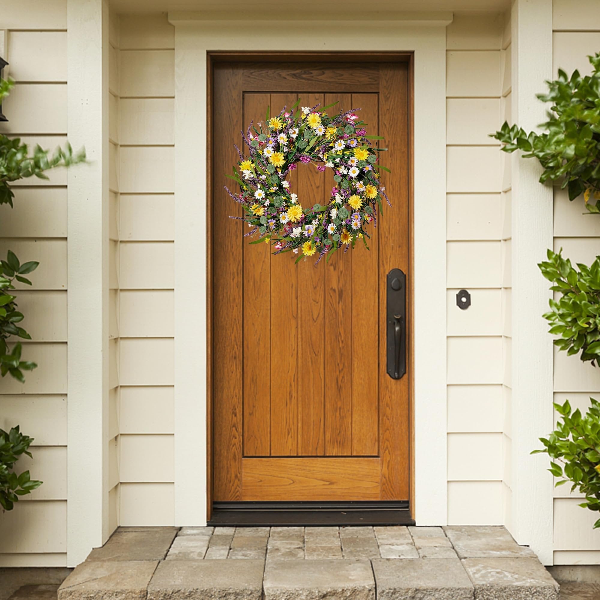 Artificial daisy and lavender wildflower wreath hanging on a wooden front door.