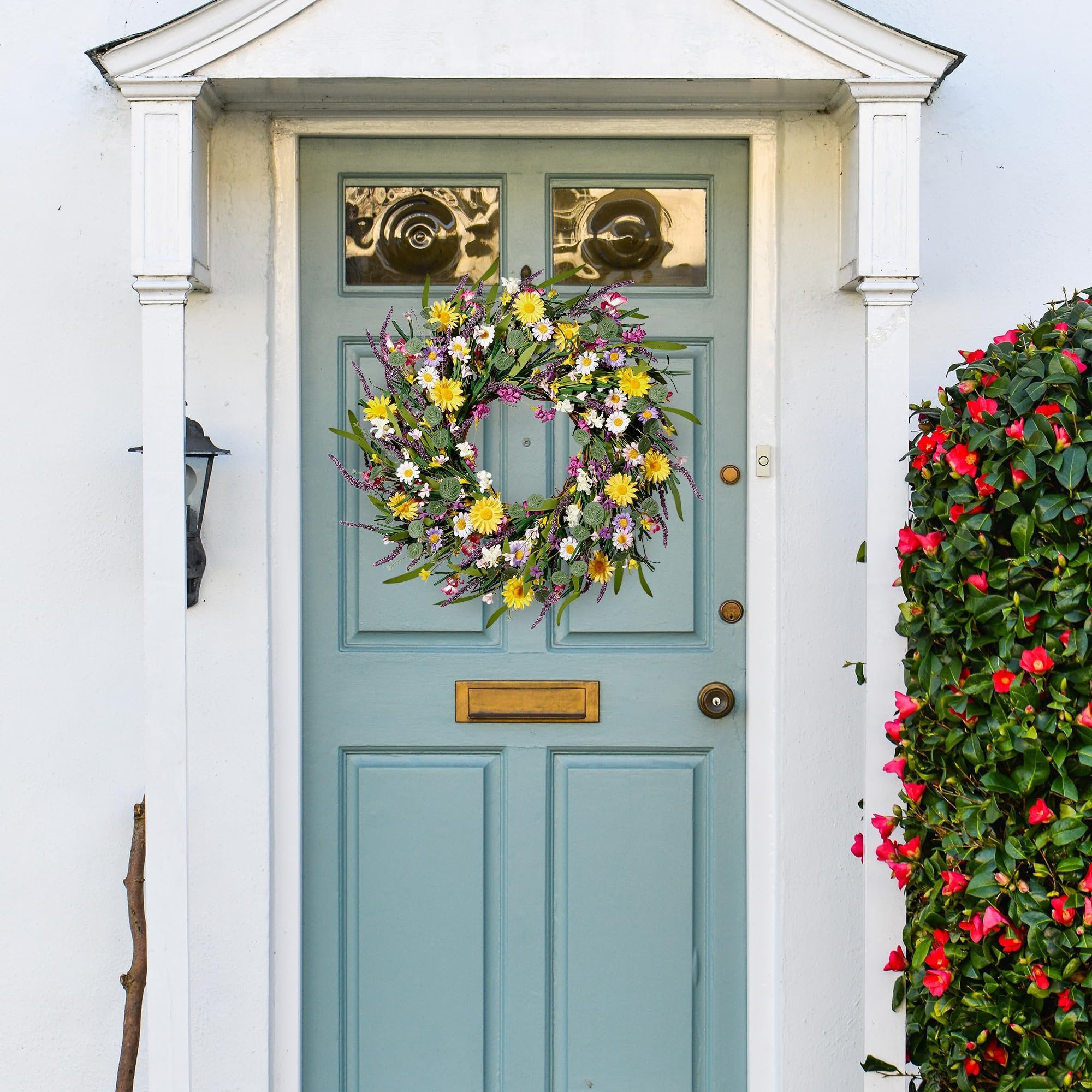 Artificial daisy and lavender wildflower wreath hanging on a light blue front door with a gold mail slot.