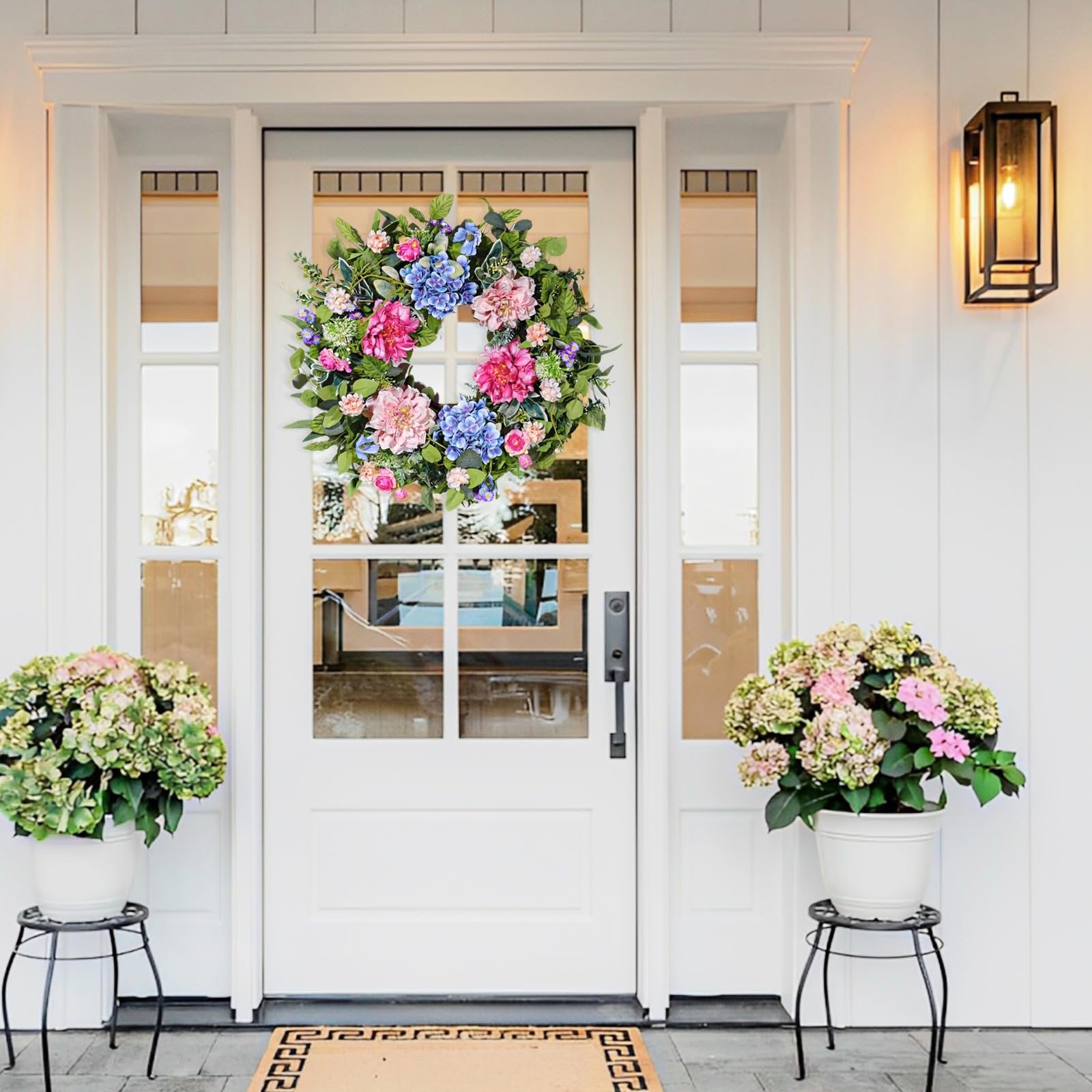 Front door decorated with a colorful floral wreath and potted plants on either side.