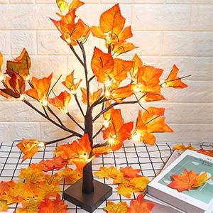 Artificial lighted maple tree with orange-red leaves and 24 LED lights, set on a checkered tablecloth with scattered leaves.