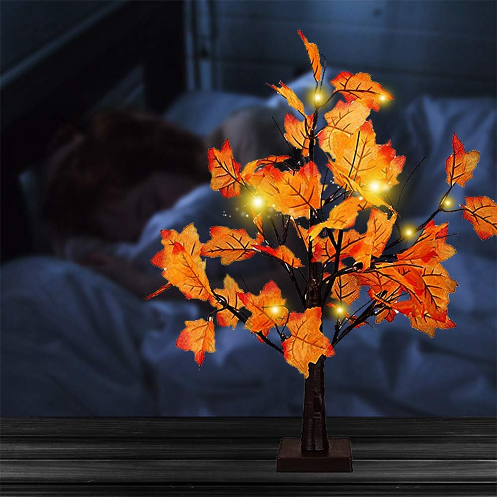 Artificial maple tree with orange-red leaves and 24 LED lights, set on a wooden surface with a blurred background of a person sleeping.