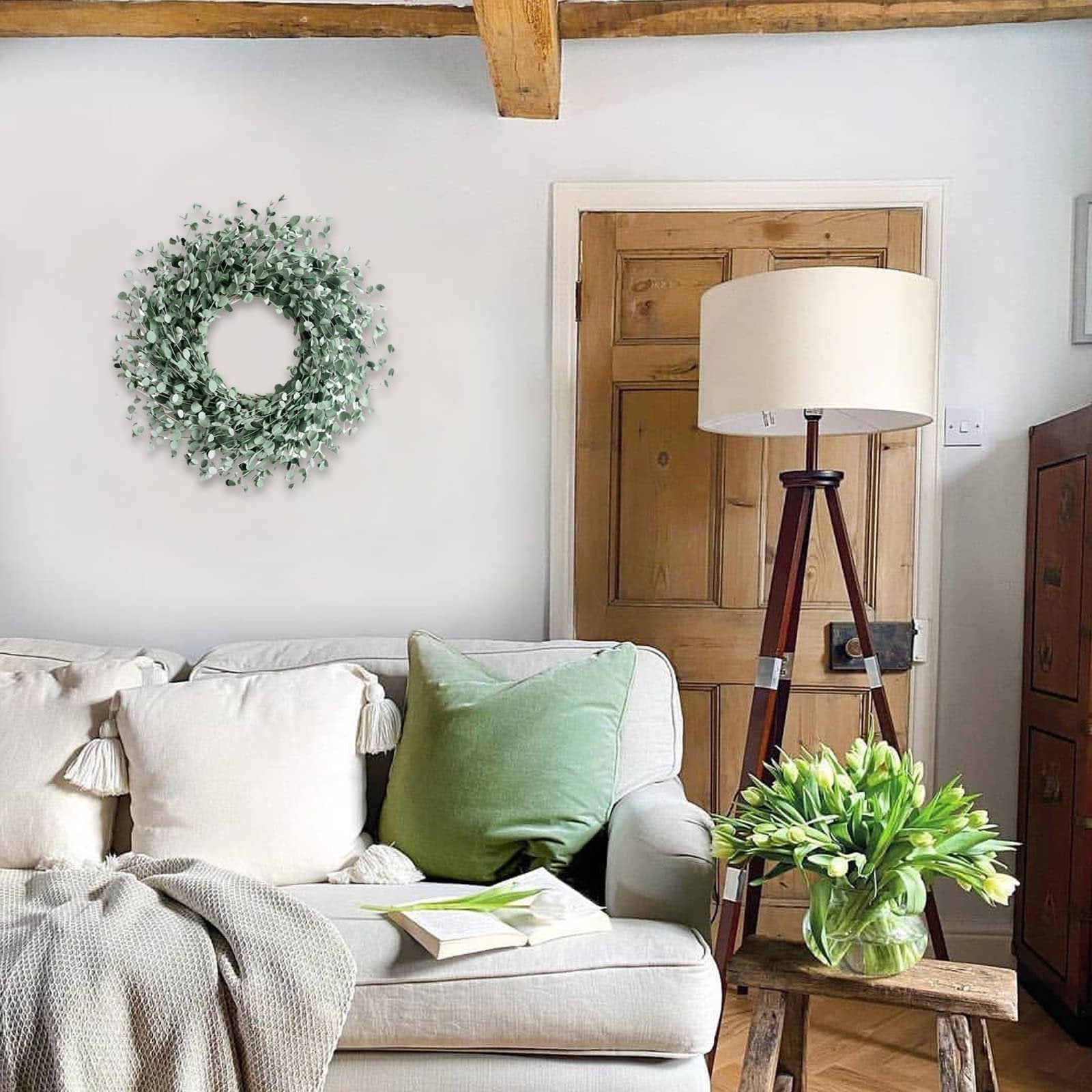 A round green wreath with small leaves hangs on a white wall above a sofa with decorative pillows and a throw blanket.
