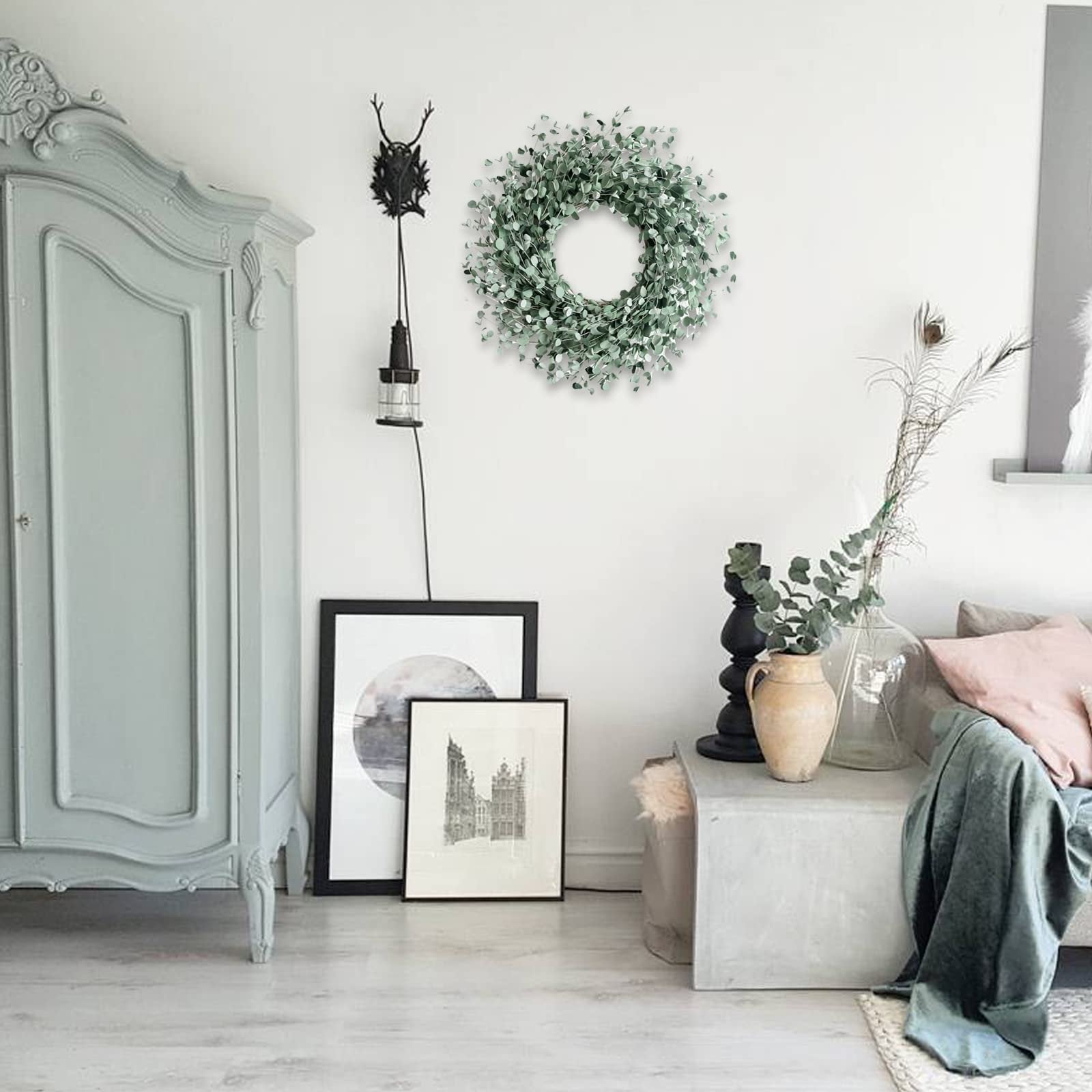 24 inch boxwood wreath with soft touch green leaves hanging on a white wall above framed art and a vintage cabinet.