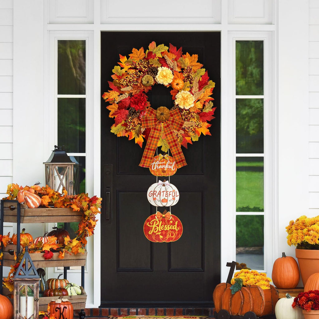 Front door decorated for fall with a large wreath, hanging pumpkin signs, and seasonal decor on a tiered stand.