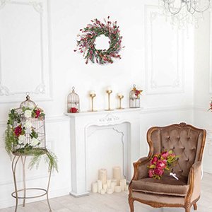 Handmade wreath with red and green foliage hanging above a fireplace with decorative elements and a chair.