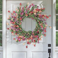 Handmade floral wreath with pink, purple, and peach flowers and green leaves hanging on a white door.