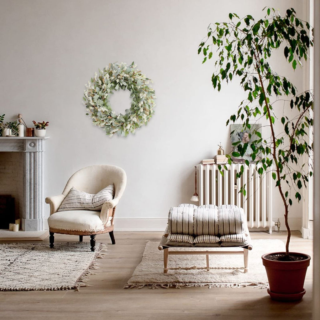 Ivory flower wreath with green lamb ear leaves hanging on a wall above an armchair in a living room setting.