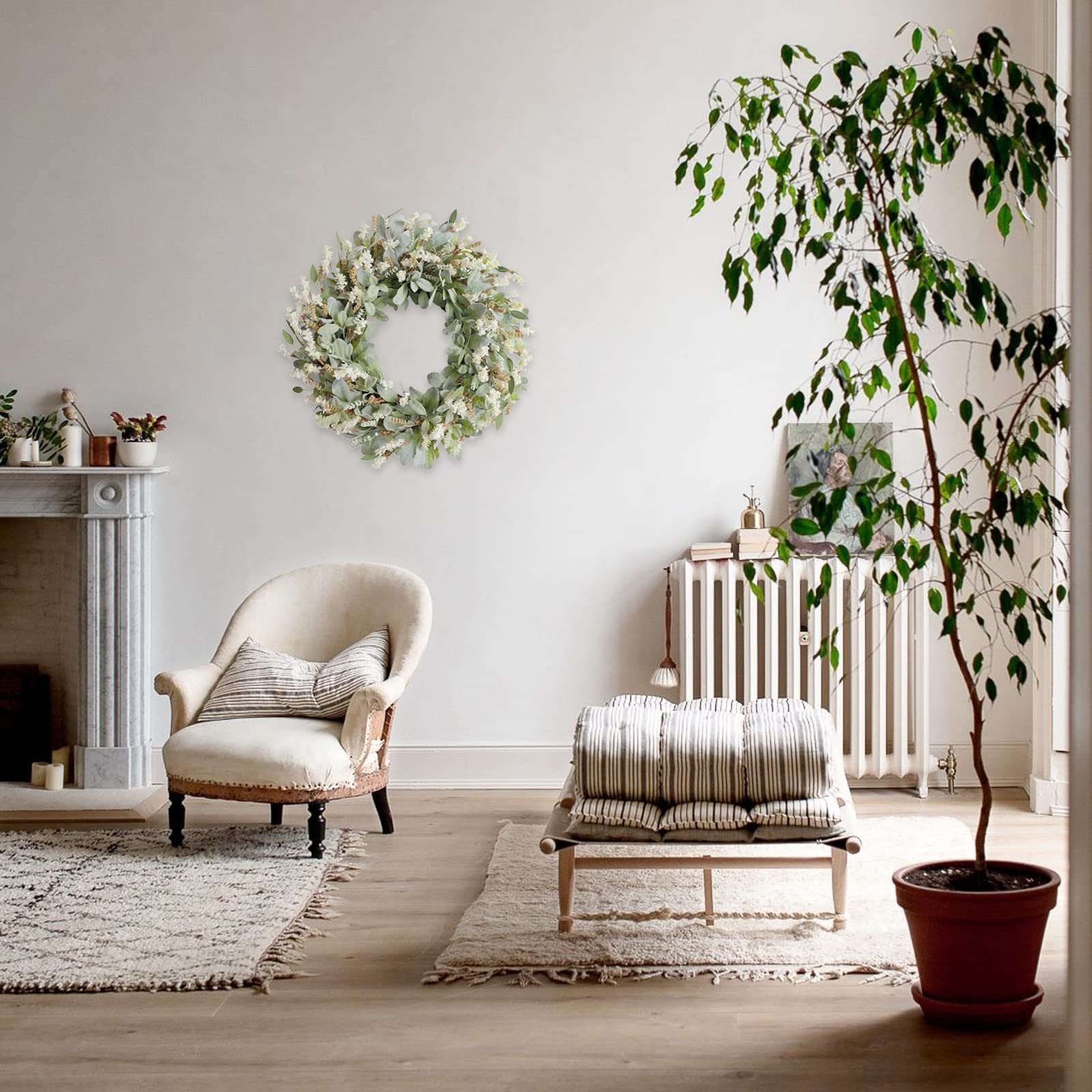 Ivory flower wreath with green lamb ear leaves hanging on a wall above an armchair in a living room setting.