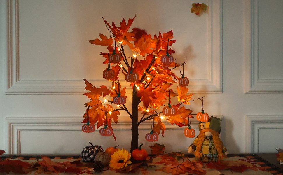 Lighted maple leaves tree with pumpkin ornaments and a gnome figure, set on a table with fall leaves.