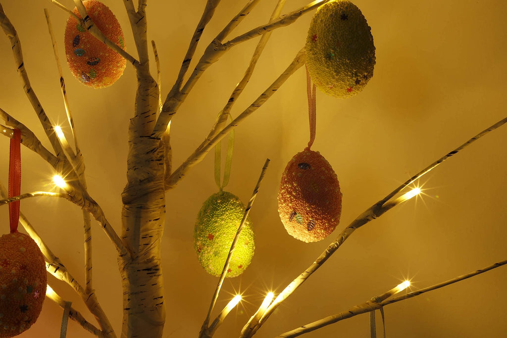 Close-up of a pre-lit white birch Easter tree with hanging egg ornaments and warm white LED lights.