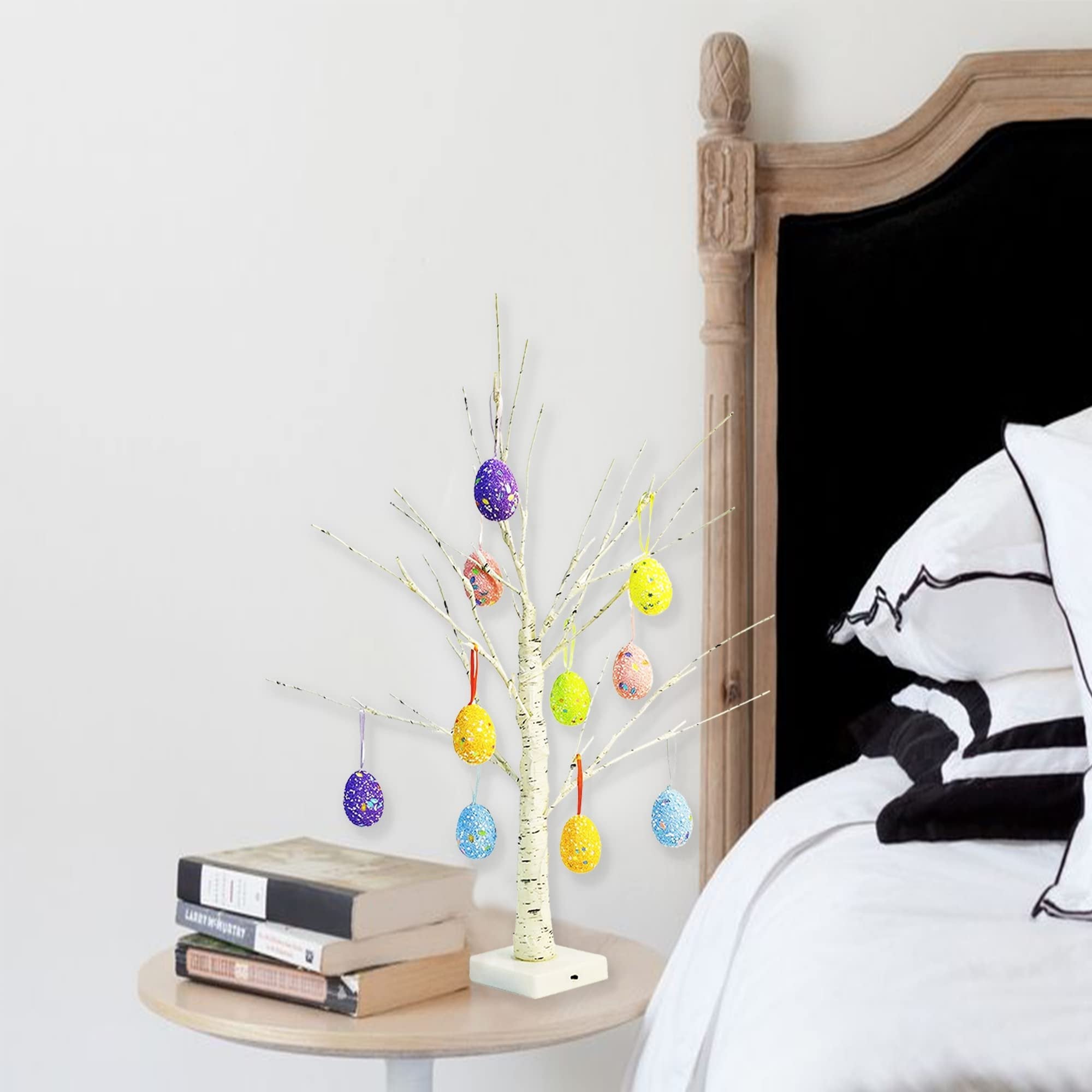 White birch Easter tree with colorful hanging egg ornaments and warm white LED lights on a bedside table.