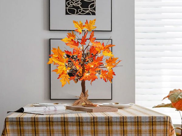 Lit artificial maple tree with orange and yellow leaves, acorns, and pine cones on a table.
