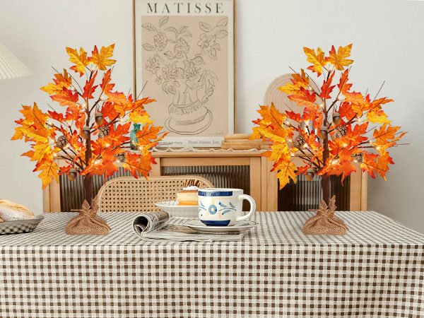 Two artificial maple trees with orange and yellow leaves, acorns, pine cones, and LED lights, set on a table.