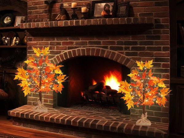 Two artificial maple trees with LED lights, acorns, and pine cones, set on a hearth in front of a fireplace.