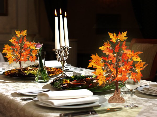 Two illuminated maple trees with acorns and pine cones on a dining table setting.
