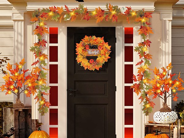 Front door decorated for autumn with lighted maple leaf garland, wreath, and trees.