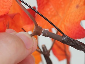 Close-up of a hand connecting wires on a decorative artificial maple tree with orange leaves.