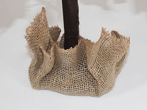Base of a decorative artificial tree wrapped in burlap, showing the trunk and burlap skirt.