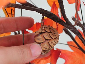 Close-up of a hand holding a pine cone ornament on a decorative maple tree with LED lights.