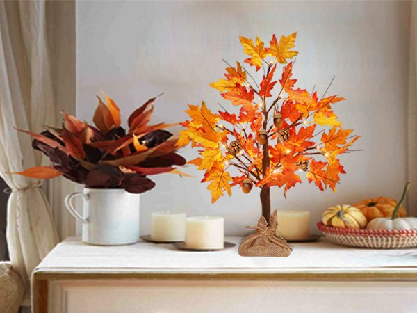 Autumn maple tree lights with acorns and pine cones, lit with warm LEDs, on a table with decorative leaves and pumpkins.