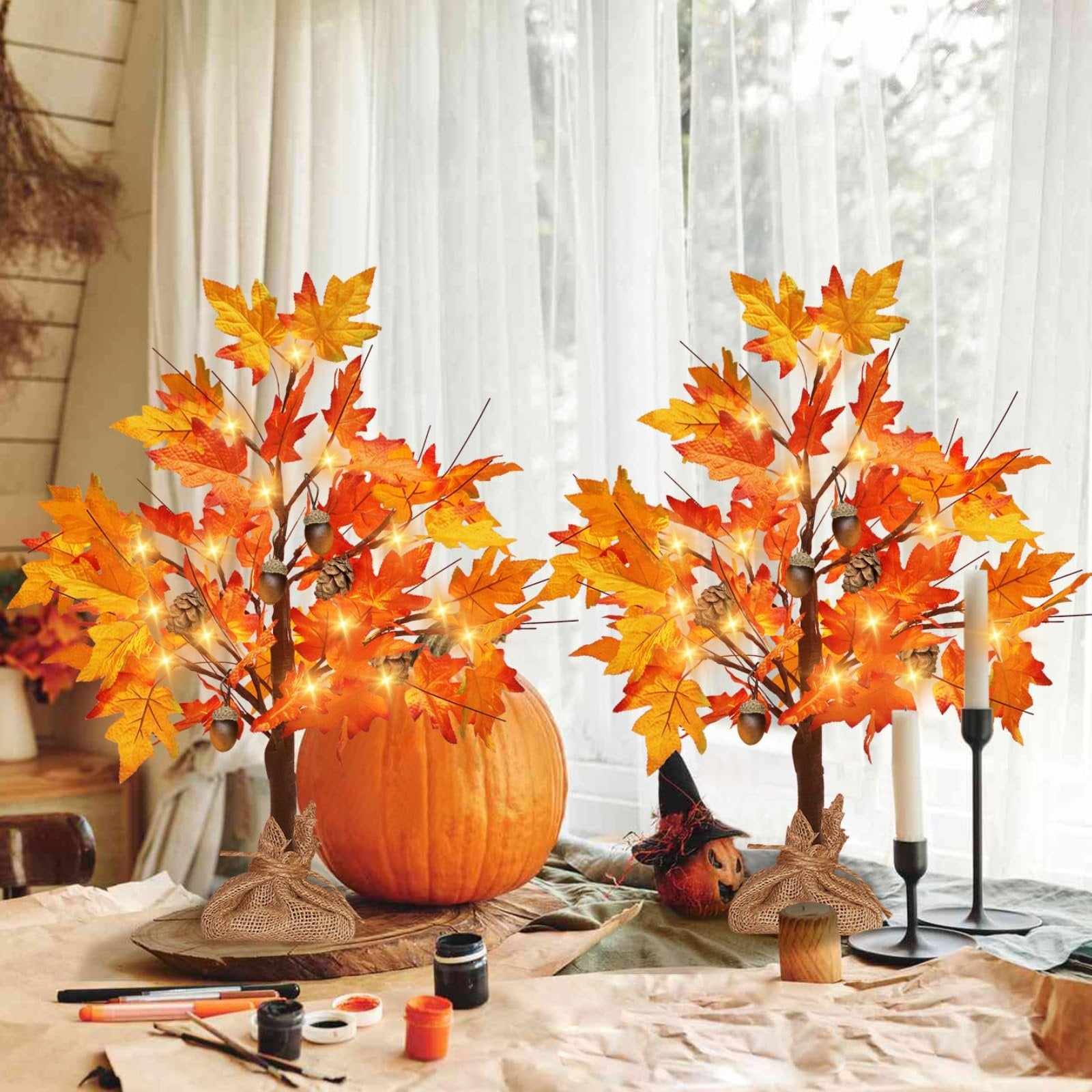 Two lighted maple trees with acorns and pine cones, set on a table with a pumpkin and craft supplies.