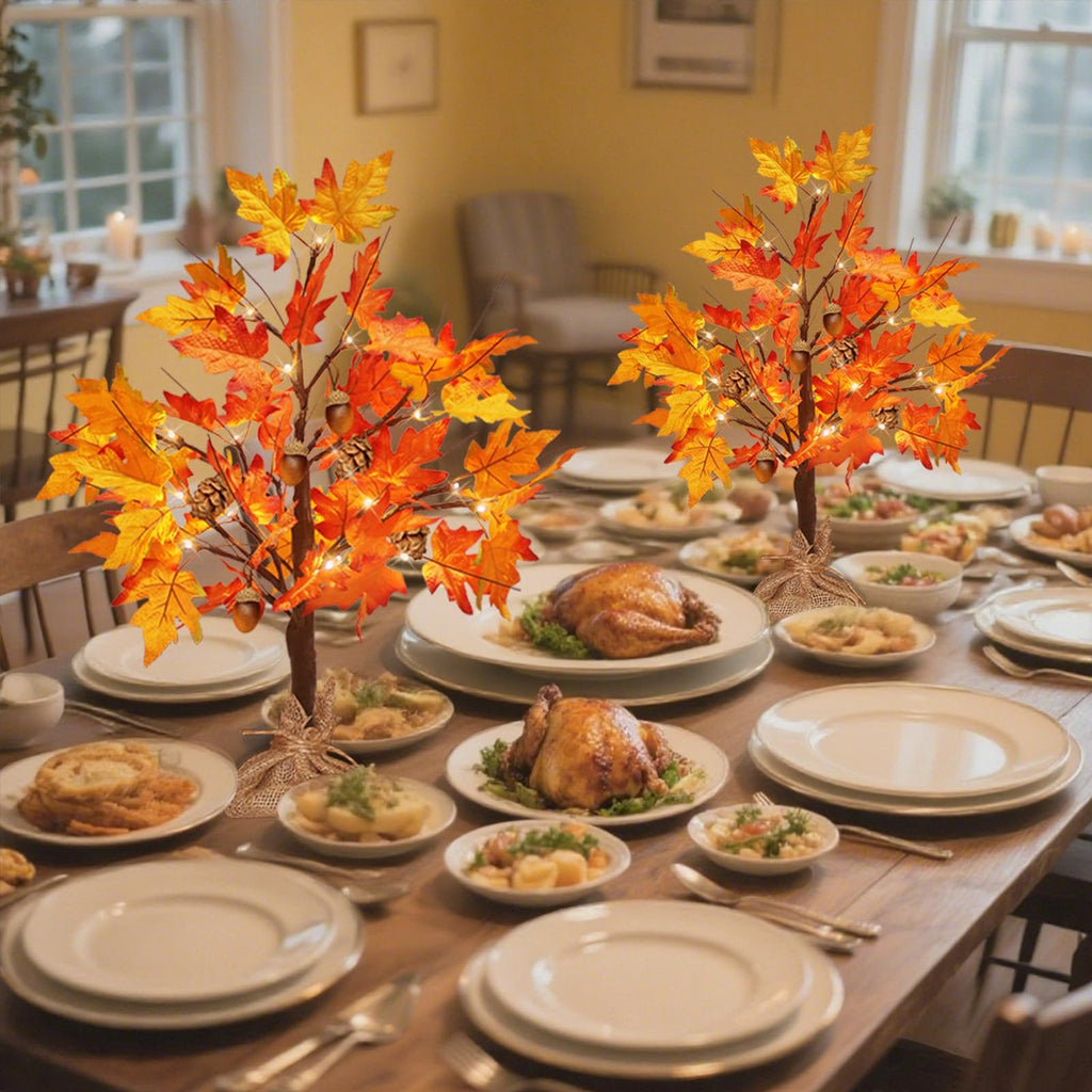 Two lighted maple trees with acorns and pine cones on a Thanksgiving dinner table setting.