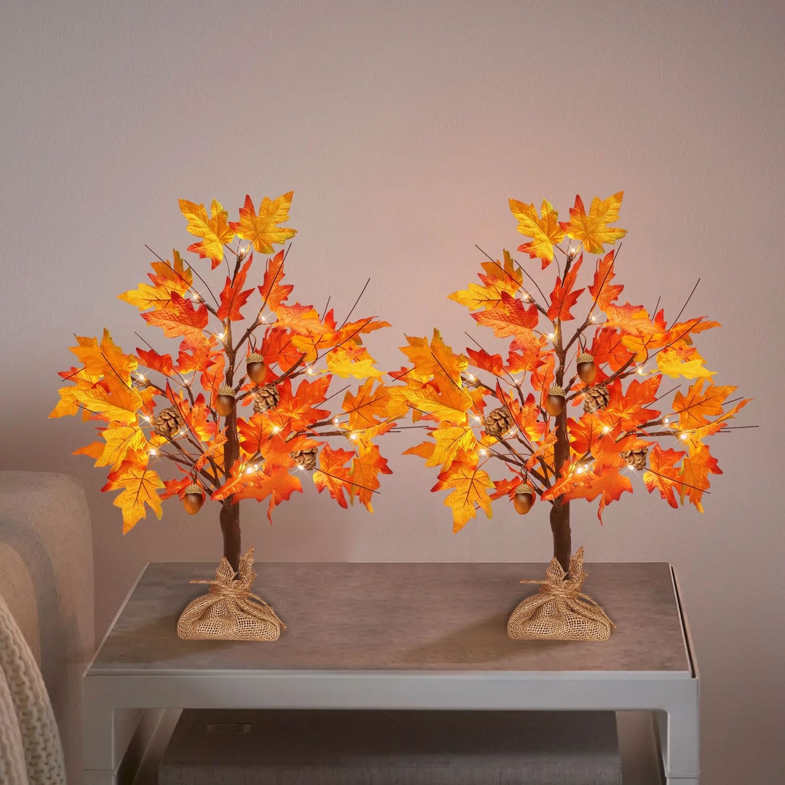 Two artificial maple trees with orange and yellow leaves, acorns, pine cones, and LED lights, on a table.