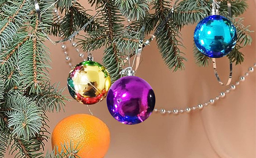 Christmas tree branches with colorful glitter ball ornaments and an orange, close-up view.
