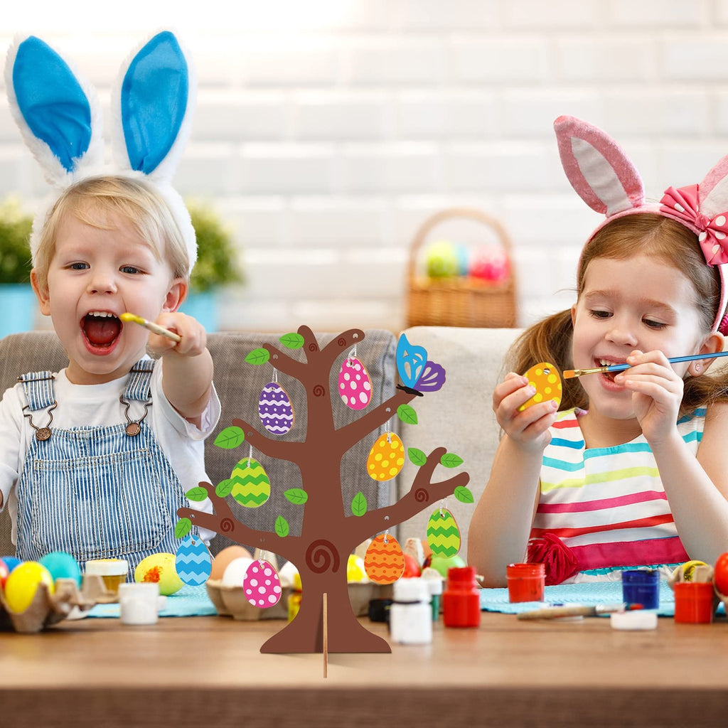 Two children painting a wooden Easter egg tree craft kit with colorful eggs and brushes.