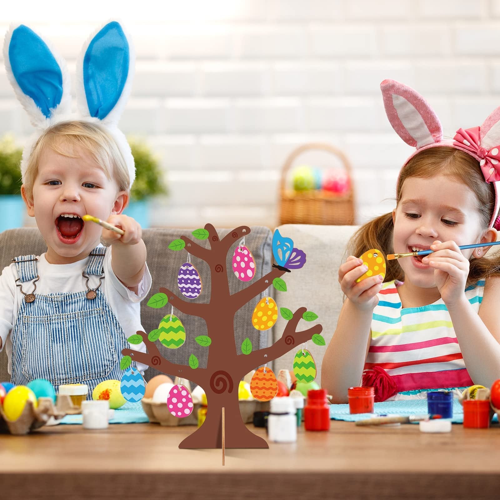 Two children painting a wooden Easter egg tree craft kit with colorful eggs and brushes.