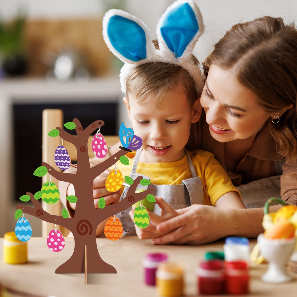 Mother and child decorating a wooden Easter egg tree craft kit with colorful egg cutouts and stickers.