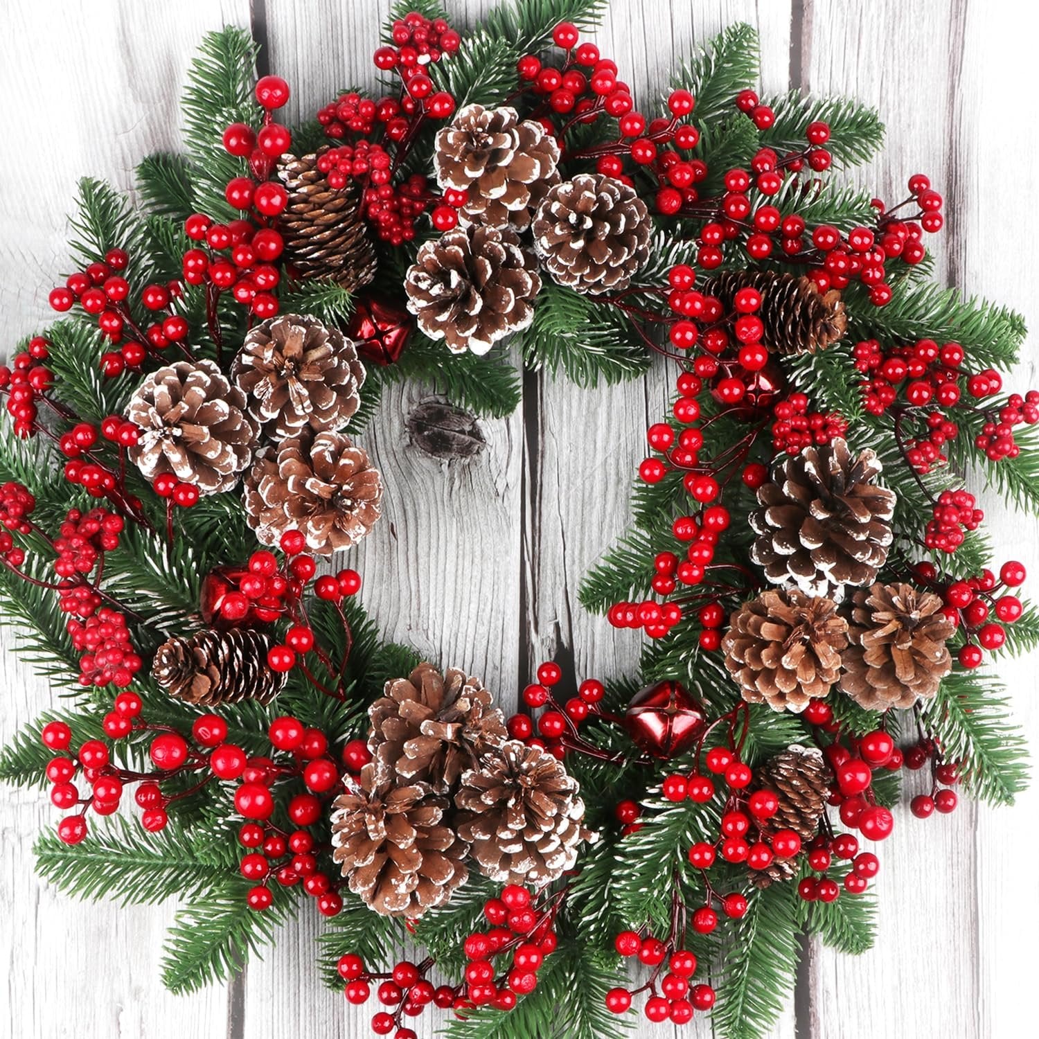 Christmas wreath with pine cones, red berries, and green pine branches on a light wood background