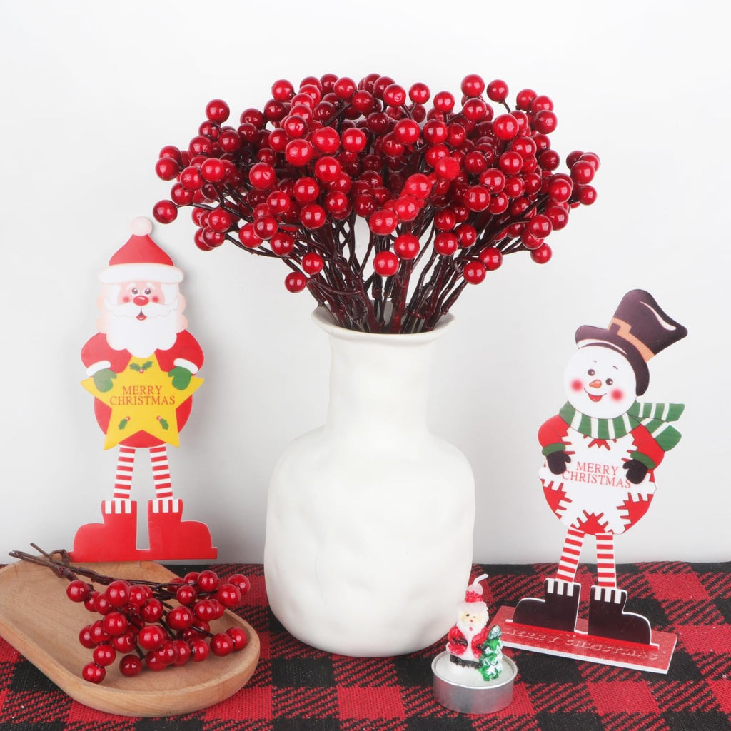 Artificial red berry stems in a white vase with Christmas decorations, including Santa and snowman figures.