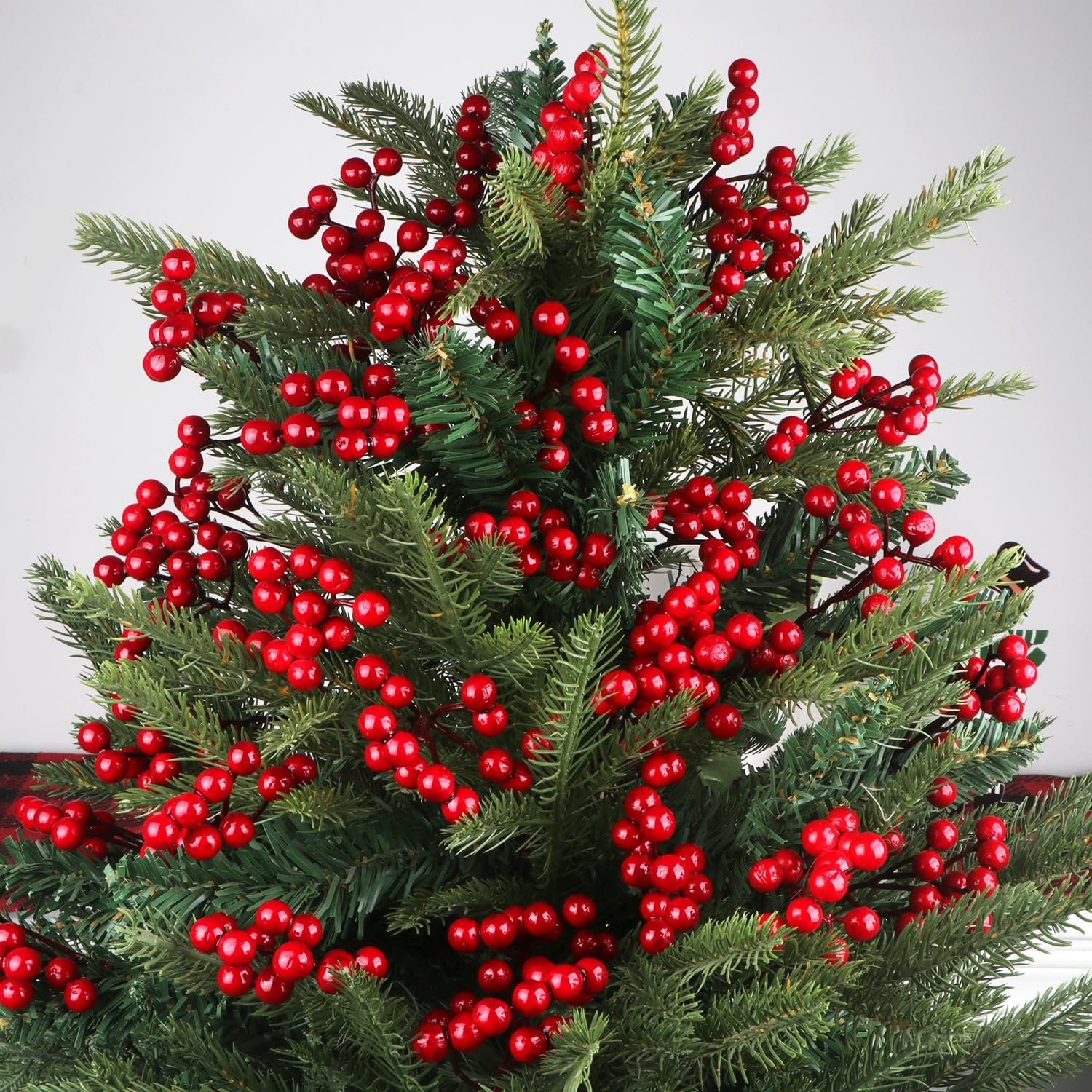 Artificial red berry stems with green pine branches, close-up view showing clusters of red berries on stems.