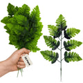Hand holding a bunch of artificial green fern fronds, with a separate frond shown on the right.