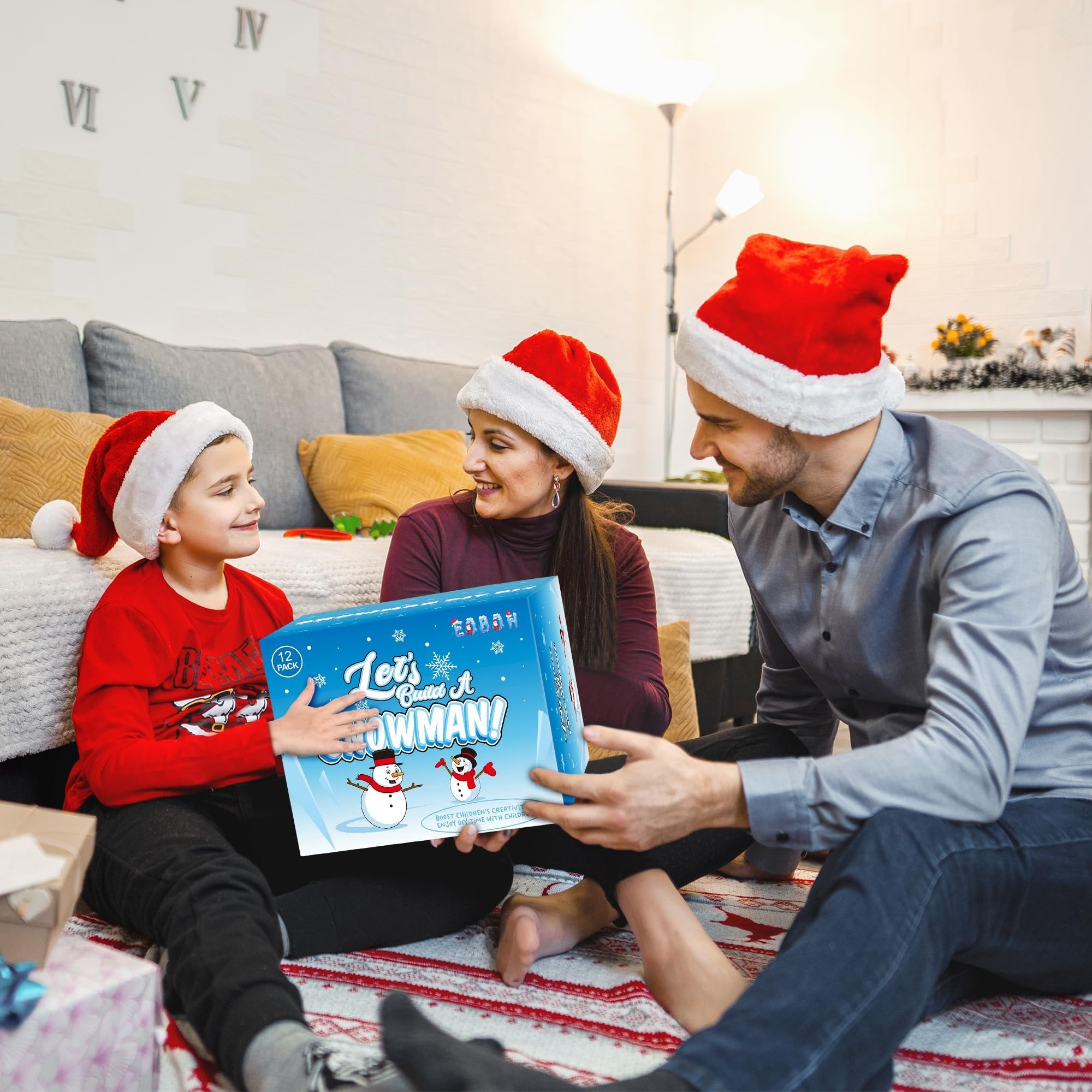 Family in Santa hats opening a 'Let's Build A Snowman!' craft kit indoors during Christmas.
