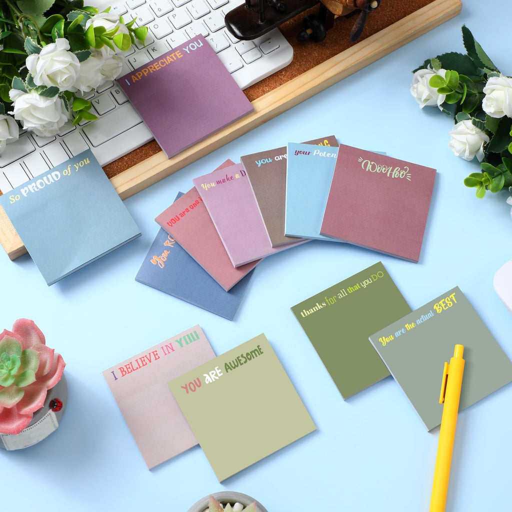 Assortment of inspirational sticky notes in various colors arranged on a desk with a keyboard and flowers.