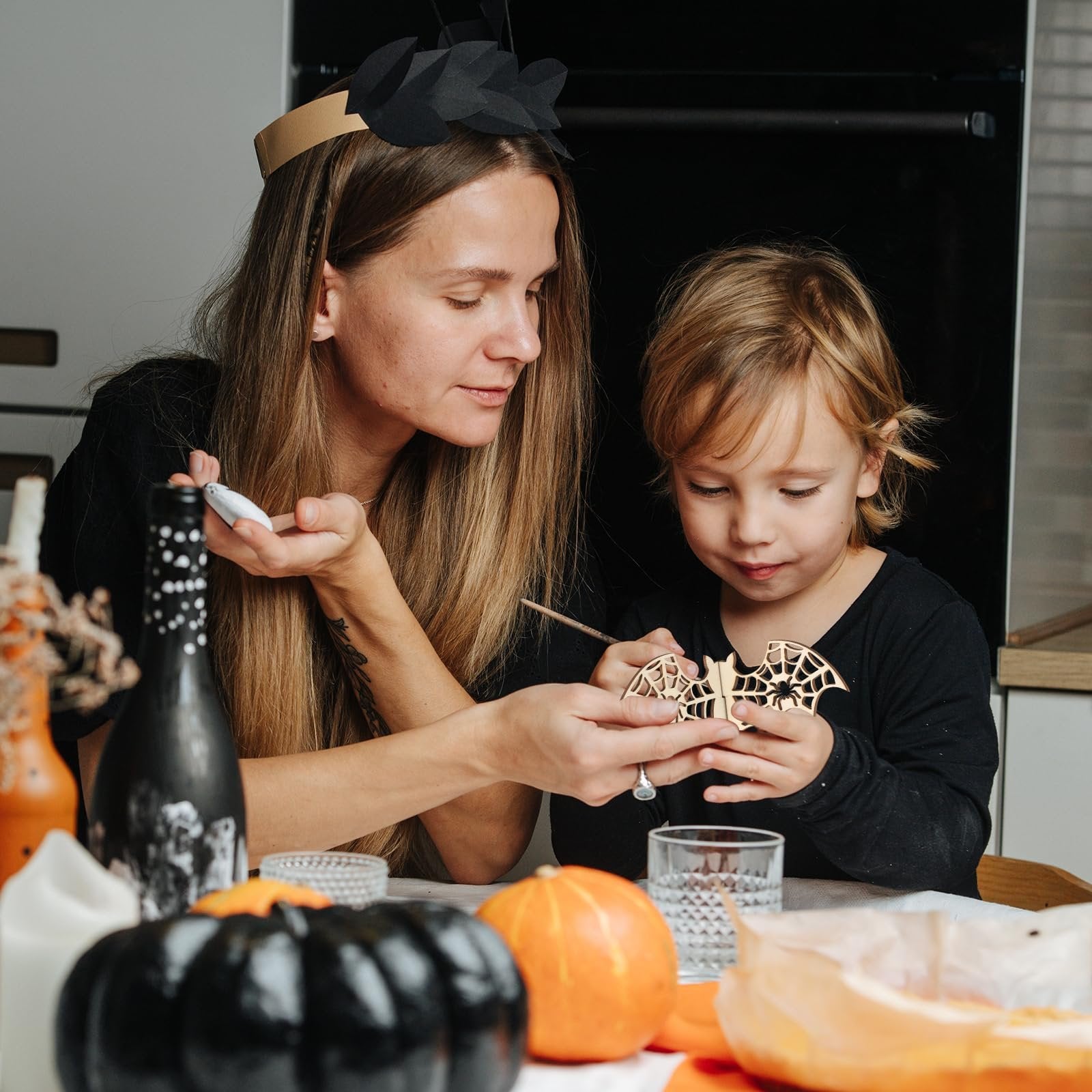 Woman and child crafting a wooden bat cutout with spiderweb design for Halloween
