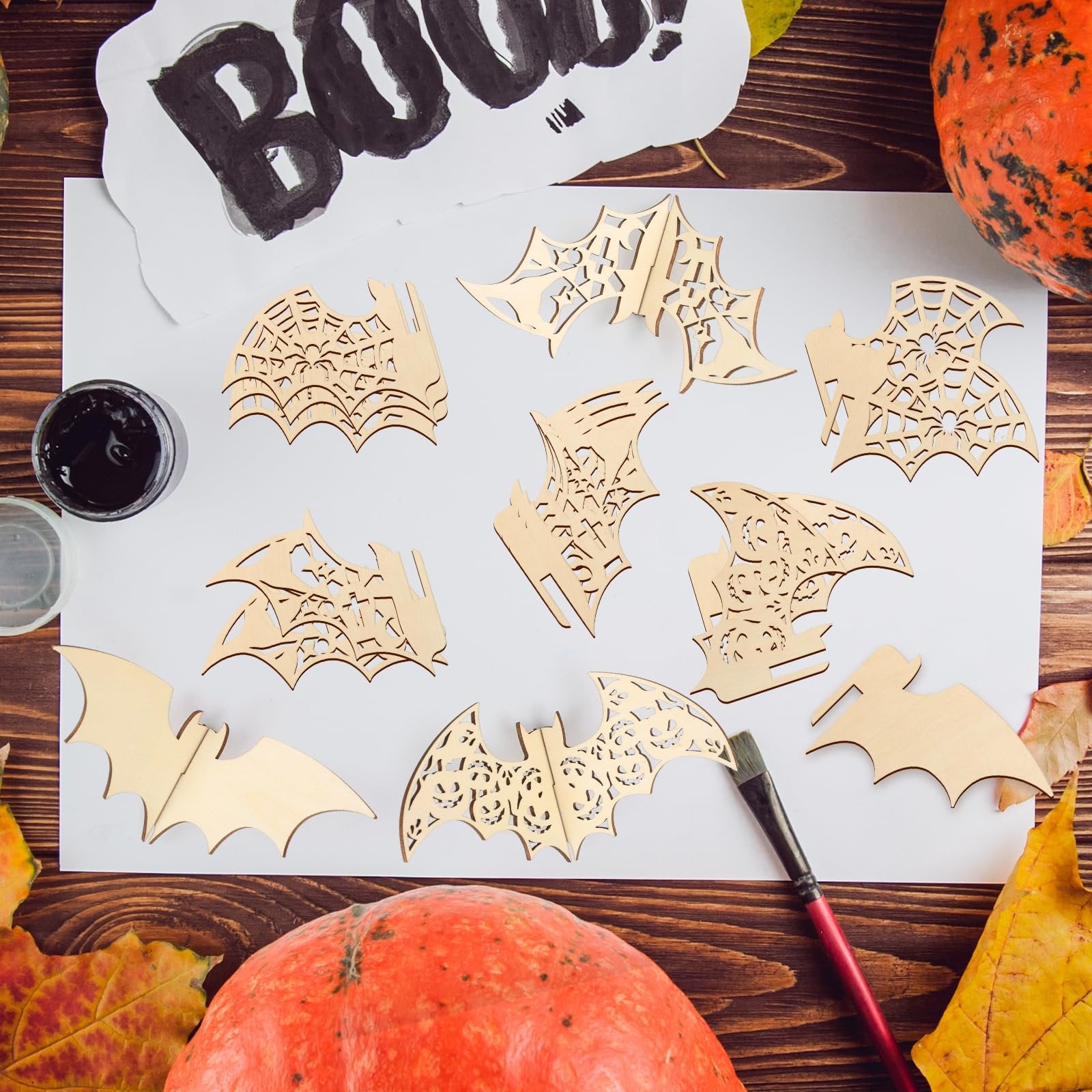 Halloween bat and spiderweb wood craft cutouts arranged on white paper with black paint and brush
