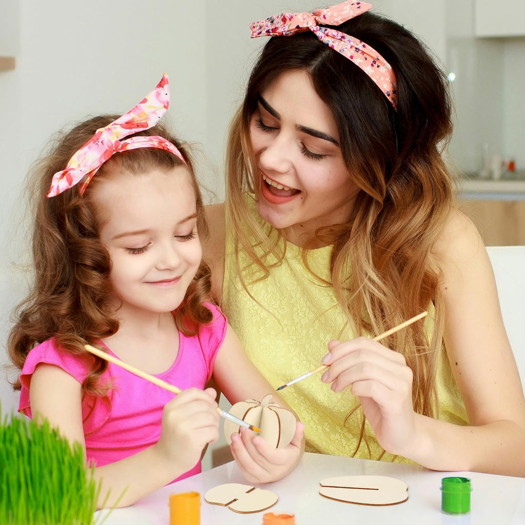 Mother and daughter painting unfinished wooden pumpkin craft pieces at a table.