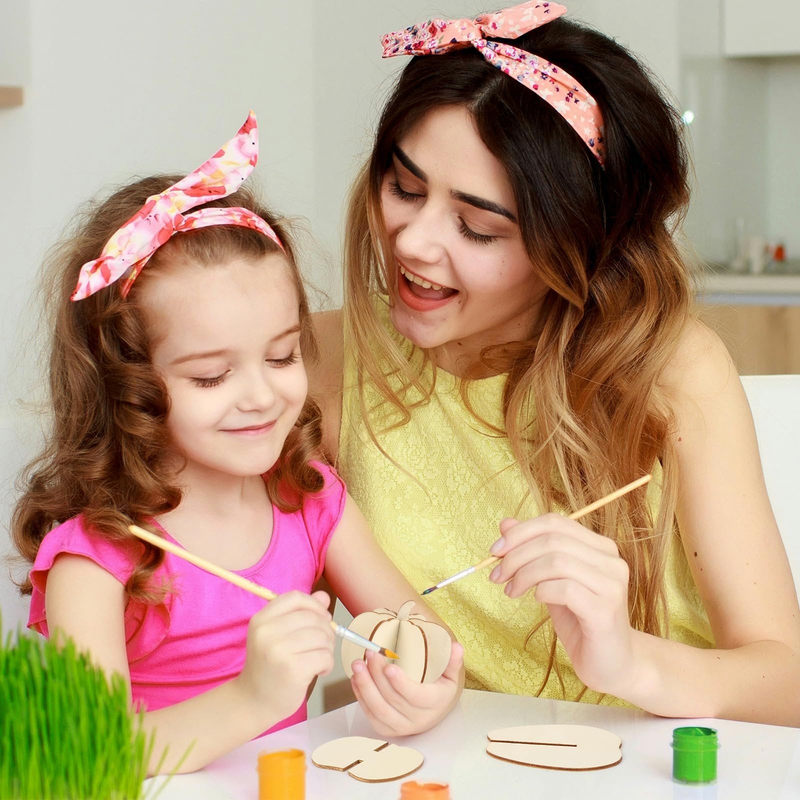 Mother and daughter painting unfinished wooden pumpkin craft pieces at a table.